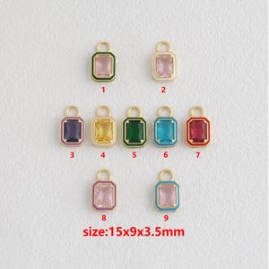 Puede incluir: Nueve colgantes rectangulares de piedras preciosas en varios colores, incluyendo rosa, verde y azul, con lazos de metal dorado. Los colgantes miden 15x9x3,5mm. Cada colgante tiene un borde de color alrededor de la gema.