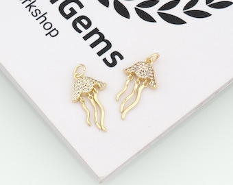 May include: Two gold-toned jellyfish charms featuring clear pavé-set stones on the bell and smooth, curved tentacles. Each charm includes a small circular jump ring at the top for attachment. The background displays the text enGems Workshop.