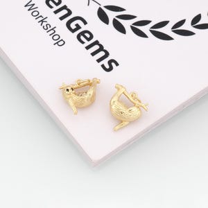 Könnte beinhalten: Zwei goldfarbene Faultier-Anhänger, die jeweils an einem Ast hängen. Ein Anhänger hat ein klares, edelsteinartiges Material auf dem Bauch. Die Anhänger befinden sich auf einer weißen Oberfläche mit dem Text "enGems Workshop".