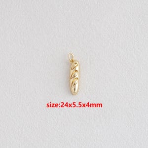Puede incluir: Un dije de baguette de color dorado con un lazo para sujetarlo a un collar o pulsera. El dije mide 24 mm de largo, 5,5 mm de ancho y 4 mm de grosor. El dije tiene tres cortes decorativos.