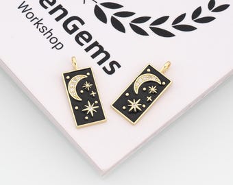 May include: Two rectangular pendants with a black background and gold trim. Each pendant features a crescent moon with embedded crystals and several star designs. The pendants have a gold loop at the top for hanging.