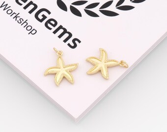 May include: Two gold starfish charms with textured detailing and small loops for attaching to jewellery. The charms are on a light pink surface with the text "menGems Workshop" in black.