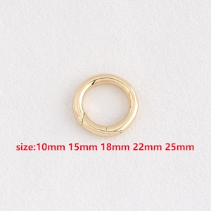 May include: A gold-colored, circular clasp with a hinged opening. The sizes available are 10mm, 15mm, 18mm, 22mm, and 25mm. The clasp is shown against a plain, off-white background.