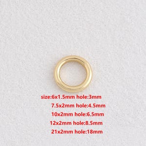 May include: A gold-coloured metal ring with a circular shape. The image text indicates various sizes, including a 6x1.5mm ring with a 3mm hole, and a 21x2mm ring with an 18mm hole. The ring is set against a light-coloured, textured background.