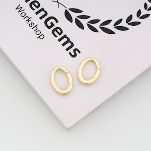 May include: Two gold-toned oval spring gate rings with a smooth, polished finish. These jewelry components feature a hinged mechanism for opening and closing, positioned on a white surface with the text "enGems Workshop" and a laurel wreath logo.