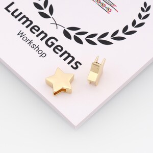 Puede incluir: Dos hallazgos de joyería de metal dorado: una estrella de cinco puntas y una pieza rectangular con dos clavijas. Los artículos están sobre una superficie blanca y rosa con el texto "LumenGems Workshop".