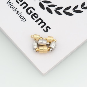 May include: A collection of magnetic jewelry clasps in gold and silver tones. The clasps are cylindrical with a magnetic closure, designed for necklaces or bracelets. The image is on a white surface with the text "enGems Workshop".