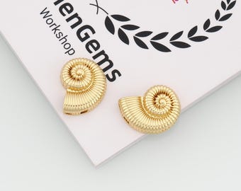 May include: Two gold-colored, seashell-shaped jewelry components. The components are detailed with spiral and ridged textures. The background is a white surface with the text "umenGems Workshop" and a decorative design.