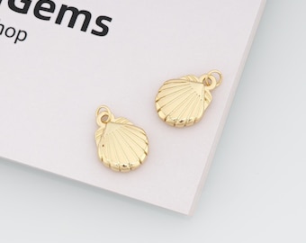 Può includere: Due ciondoli a forma di conchiglia color oro con superficie strutturata e un piccolo anello nella parte superiore per il fissaggio. I ciondoli sono su una superficie bianca. La parola "Gems" è visibile sullo sfondo.