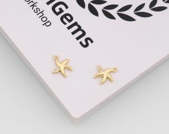 May include: Two gold starfish charms, each with a small clear gem. They rest on a white surface with the text "enGems Workshop" in black. The charms are likely for jewellery.
