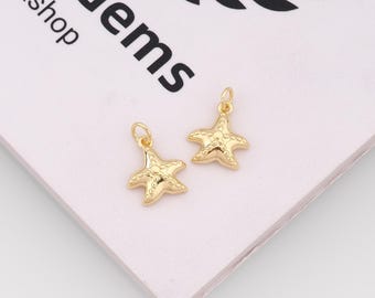 May include: Two gold-toned starfish charms, each featuring a small jump ring at the top for attachment. The starfish have a textured, raised surface detail. The background displays partial black text reading "Gems" and a laurel wreath graphic.