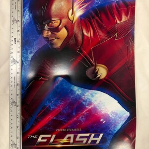 May include: A poster featuring The Flash in a red and gold costume, with a dynamic pose against a blue and red background. The title "THE FLASH" is prominently displayed, with the text "Tuesdays 8/7c CW" below.
