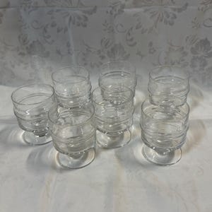 Pode incluir: Conjunto de oito copos de beber de vidro transparente com um design texturizado. Os copos têm uma base redonda e uma tigela larga.