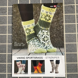 May include: A pair of knitted socks with a green, white, and yellow snowflake pattern. The socks are displayed on a magazine cover with the text "VIKING DESIGN" and "VIKING SPORTSRAGG - STRØMPER".