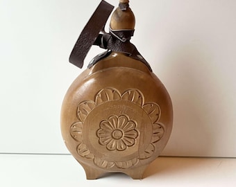 Könnte beinhalten: Eine Holzflasche mit einem geschnitzten Blumenmuster und einem braunen Lederriemen.