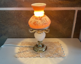 Lámpara de mesa estilo huracán vintage con pantallas de cristal floral, base ornamentada de latón fundido y mármol blanco.