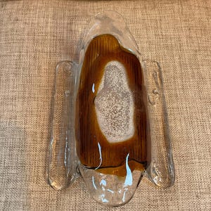 May include: A clear glass wall sconce with a brown and white interior. The sconce has two clear glass extensions on either side. The interior has a textured appearance. The sconce is designed to be mounted on a wall.