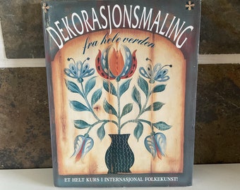 Könnte beinhalten: Ein Buchcover mit einem Gemälde von Blumen in einer Vase. Der Titel des Buches lautet "Dekorasjonsmaling fra hele verden" und der Text unter dem Gemälde lautet "Et helt kurs i internasjonal folkekunst!"