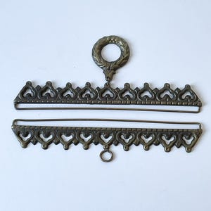 May include: Two antique bronze-colored metal jewelry findings. The top piece has a decorative wreath and a row of heart-shaped cutouts. The bottom piece has a row of heart-shaped cutouts and a small ring. Both pieces are connected by a thin metal bar.