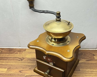May include: A vintage wooden coffee grinder with a brass top and a hand crank. The grinder has a drawer for collecting coffee grounds and a floral design painted on the side.