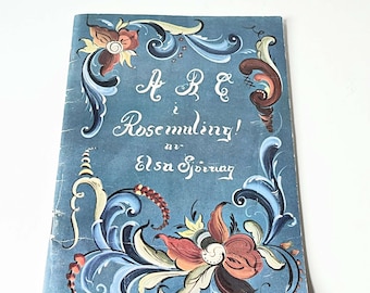 May include: A blue book with a title that reads "ABC i Rosemåling! av Elsa Sjörang". The cover features a floral design with blue, yellow, red, and white colors.