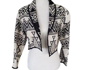 May include: A cropped black and white patterned cardigan with a shawl collar. The cardigan is made of a soft, woven fabric and has a relaxed fit.