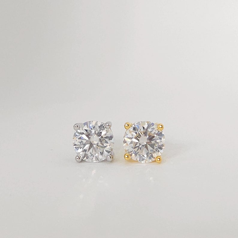 May include: Two round-cut diamond stud earrings. One earring has a silver setting, and the other has a gold setting. The diamonds are clear and sparkling, set with four prongs.