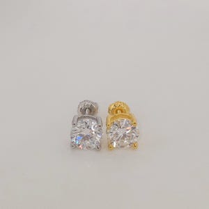 May include: Two stud earrings, one silver and one gold, each with a large, round, clear gemstone. The earrings are displayed against a plain, light background, highlighting their sparkling facets and classic design.