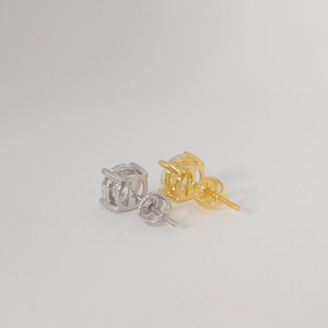 May include: A pair of stud earrings, one silver and one gold, each with a round, clear gemstone. The earrings have a four-prong setting, with a post and butterfly clasp.