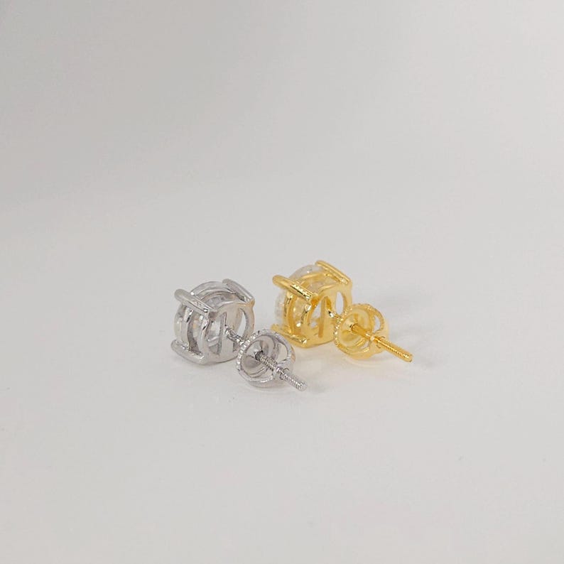May include: A pair of stud earrings, one silver and one gold, each with a round, clear gemstone. The earrings have a four-prong setting, with a post and butterfly clasp.