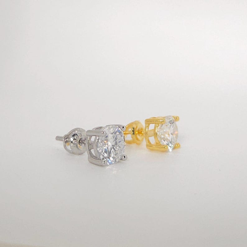May include: Two stud earrings, one silver and one gold, each with a large, round, clear gemstone. The earrings are displayed against a plain white backdrop, emphasising their sparkle and design.