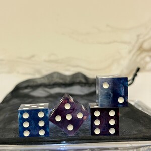 May include: Four dice with a swirling blue and purple marbled pattern. The dice have white dots on each side.