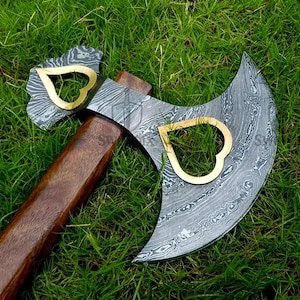 Peut inclure: Une hache en acier de Damas avec un manche en bois. La tête de la hache présente un motif et deux découpes dorées en forme de cœur. Le manche est de couleur marron foncé.