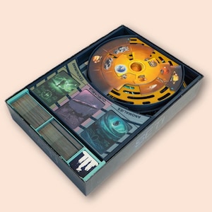 May include: A board game box with a circular game board and various cards. The game board is yellow and brown with illustrations of planets and figures. The box contains cards with images and text, and the word "SETI" is visible on the box.