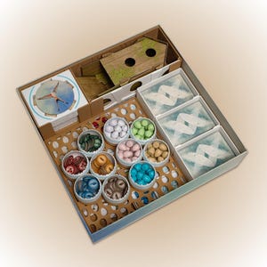 May include: A board game organizer with various components. It includes wooden game pieces, cards, and containers filled with colorful tokens. The organizer is designed to hold game pieces and cards, keeping them organized and accessible.