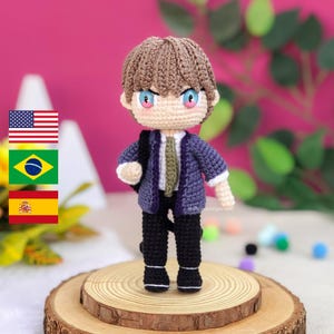May include: Crocheted amigurumi doll with brown hair, a purple jacket, a green tie, and black pants. The doll is standing on a wooden platform.