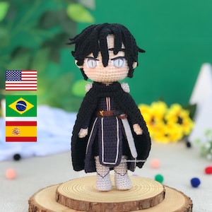 Pode incluir: Boneca de crochê feita à mão de um personagem com cabelo preto, usando uma capa preta e uma roupa azul escura. A boneca tem olhos brancos e está em pé sobre uma fatia de madeira. A boneca tem cerca de 15 cm de altura.