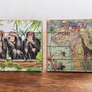 Könnte beinhalten: Zwei dekorative Holzblöcke. Einer zeigt drei Affen in der Pose „Nichts sehen, nichts hören, nichts sagen“. Der andere Block zeigt eine Vintage-Karte von Afrika mit einer Giraffe.