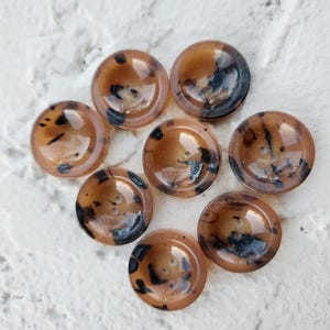 May include: Eight brown and black patterned buttons with a raised centre. The buttons are round and have a glossy finish.