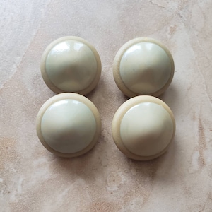 May include: Four beige buttons with a white center and a raised dome shape.