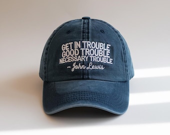 May include: A navy blue baseball cap with the quote "GET IN TROUBLE GOOD TROUBLE NECESSARY TROUBLE - John Lewis" embroidered in white. The cap has a curved brim and an adjustable strap.
