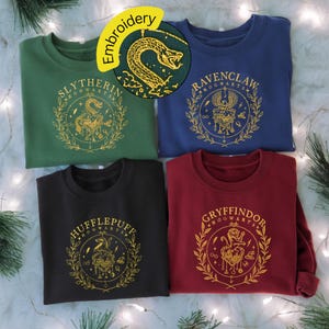 May include: Four crewneck sweatshirts in green, blue, black, and red. Each sweatshirt features a gold embroidered crest with the names of Hogwarts houses: Slytherin, Ravenclaw, Hufflepuff, and Gryffindor. The word "Embroidery" is in a yellow circle.