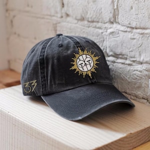May include: A black baseball cap with a curved brim. The cap features a gold embroidered sunburst design on the front and the number "33" on the side. The cap is made of a soft, worn material.