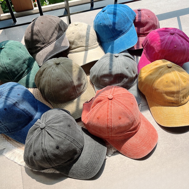 Puede incluir: Una colecci&oacute;n de doce gorras de b&eacute;isbol en varios colores, incluyendo gris oscuro, verde bosque, azul marino, beige, azul brillante, granate, magenta, gris, amarillo mostaza y coral. Cada gorra presenta un dise&ntilde;o de seis paneles.