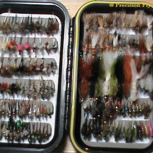 May include: Two black fly fishing boxes filled with a variety of colorful flies. The boxes are labeled "Precision Fly & Tackle".