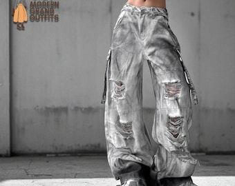 May include: Grey distressed denim trousers with multiple large rips and a wide leg. The trousers have a faded, worn look and feature straps on the sides. The text "Modern Grand Outfits" is visible in the upper left corner.