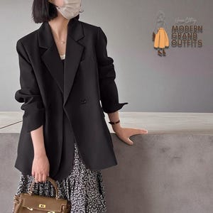 May include: A black blazer with a double-breasted design, paired with a floral print skirt and a brown handbag. The blazer has a classic lapel and is worn with the sleeves rolled up. The image also includes the text "Unique City MODERN GRAND OUTFITS".
