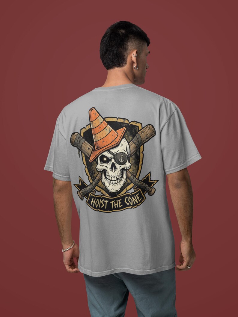 May include: A light gray t-shirt featuring a skull wearing an orange traffic cone and an eye patch. The skull is set against a shield with crossed baseball bats and the text "HOIST THE CONE".