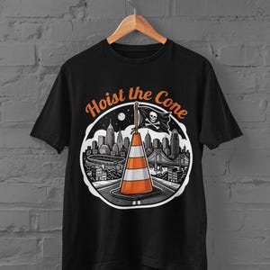 K&ouml;nnte beinhalten: Schwarzes T-Shirt mit einer Grafik einer Verkehrskegel, einer Piratenflagge und einer Stadtlandschaft. Der Text "Hoist the Cone" ist &uuml;ber dem Bild angeordnet. Das Design verwendet Orange, Wei&szlig; und Schwarz.
