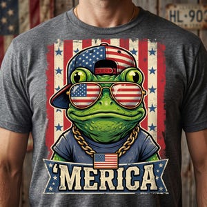 Peut inclure: Un t-shirt gris anthracite avec un motif de grenouille verte portant une casquette à motif de drapeau américain, des lunettes de soleil aux verres étoilés et rayés, et une chaîne dorée avec un pendentif drapeau. Une bannière affiche 'MERICA.